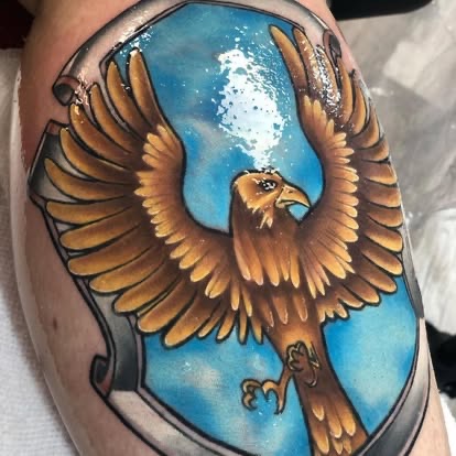 Neo-traditional golden eagle crest tattoo on a blue shield background